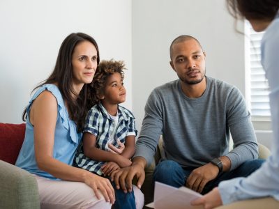 Serious couple with son in a deep conversation with family counselor. Multiethnic parents talking about adoption with their counselor. Family at the financial planning consultation.